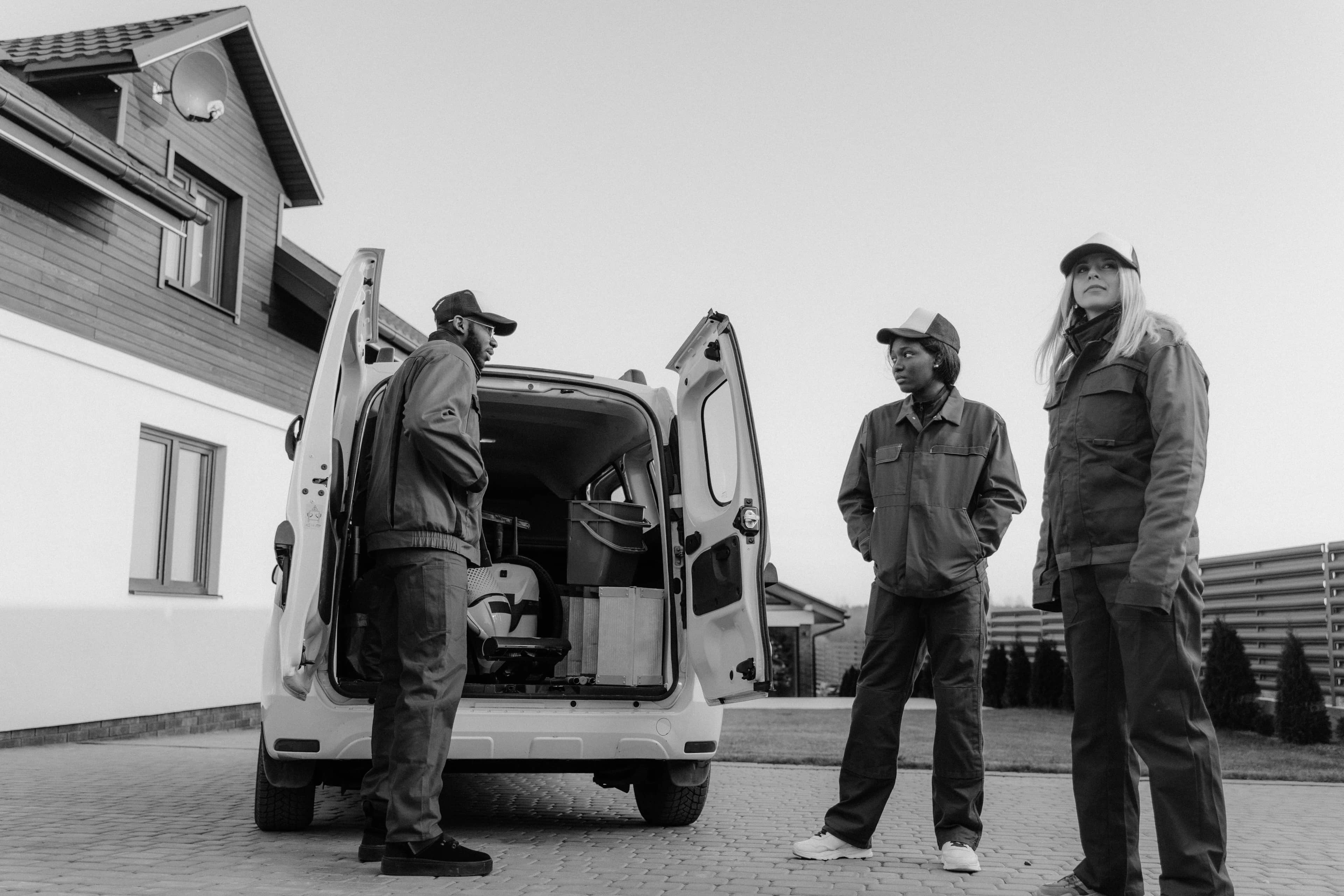 Three workers in coveralls unloading equipment from a van